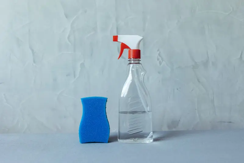 Sprühflasche und blauer Schwamm auf grauem Hintergrund